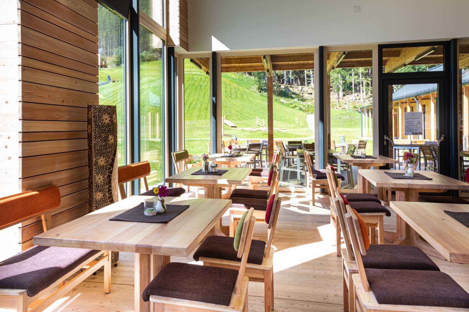 Heller Restaurant-Innenraum mit Panoramafenstern und Blick auf die Almwiese